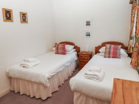 A bedroom with two single beds with white linens and plaid pillows and a wooden nightstand between the beds with pictures on the wall and floral curtains at Lavender cottage in Akeld near Wooler