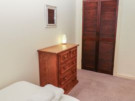 A wooden chest of drawers with a lamp on top beside a wooden closet door with louvers and a bed with white towels in a room at Lavender cottage in Akeld near Wooler