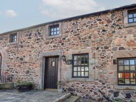 Stone cottage exterior with three windows and a dark wooden door with plants outside at Freesia Cottage Akeld near Wooler