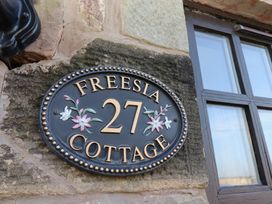An oval black plaque with the number 27 and flowers on a stone wall near a window at Freesia Cottage Akeld near Wooler