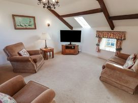 A living room with upholstered chairs a sofa a television on a wooden stand and a small window with curtains at Freesia Cottage in Akeld near Wooler