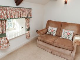 A room with a brown sofa with floral cushions and a window with floral curtains at Freesia Cottage Akeld near Wooler