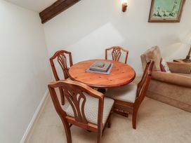 A small dining area with a round wooden table and four wooden chairs next to a beige sofa and a framed picture on the wall at Freesia Cottage Akeld near Wooler