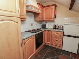 A kitchen with wooden cabinets a stovetop oven a microwave kettle toaster and a refrigerator at Freesia Cottage Akeld near Wooler