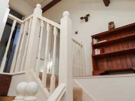 A staircase with white wooden railing and a wooden bookshelf with books and an owl ornament at Freesia Cottage in Akeld near Wooler