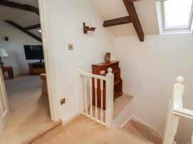 A landing area with a wooden shelf and an owl figurine next to a staircase and a doorway leading to a room with a TV and furniture at Freesia Cottage Akeld near Wooler
