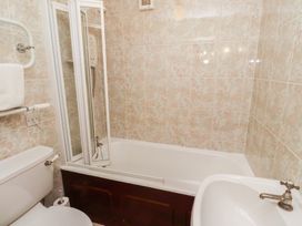 A bathroom with a toilet, bathtub with shower screen, sink, towel rail, and tiled walls at Freesia Cottage Akeld near Wooler