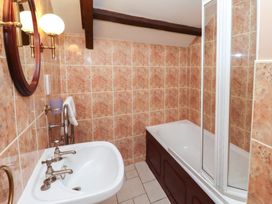 A bathroom with a sink, bathtub with glass shower screen, round mirror, wall lights, and a towel on a rail at Freesia Cottage Akeld near Wooler