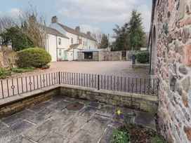 A stone patio with a metal railing next to a stone wall and a gravel driveway with white houses and bushes in the background at Freesia Cottage Akeld near Wooler