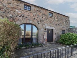 Stone exterior of a building with arched windows and a black door with bushes in front at Aubretia Trail in Akeld near Wooler