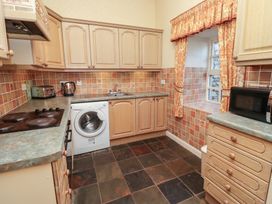 A kitchen with wooden cabinets and tiled walls featuring a washing machine toaster microwave and window with curtains at Aubretia Trail Akeld near Wooler