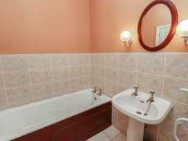 A bathroom with a bathtub a sink an oval mirror and two wall lights at Aubretia Trail Akeld near Wooler