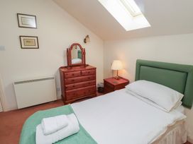 A bedroom with a single bed with green headboard a wooden dresser with mirror and a nightstand with lamp at Aubretia Trail in Akeld near Wooler