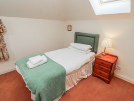 A single bed with green headboard and blanket next to a wooden nightstand with a lamp at Aubretia Trail Akeld near Wooler