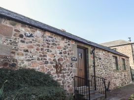 A stone exterior wall with a brown wooden door and windows at Bizzie Lizzie in Akeld near Wooler
