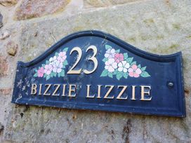 A house number sign 23 with floral design and the name Bizzie Lizzie on a stone wall at Bizzie Lizzie in Akeld near Wooler