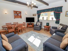 A living room with a dining table chairs armchairs a rug and a television at Bizzie Lizzie in Akeld near Wooler