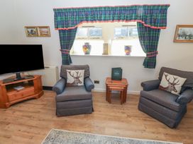 A living room with two armchairs a television on a wooden stand and a small table under a window with blue and green curtains at Bizzie Lizzie in Akeld near Wooler