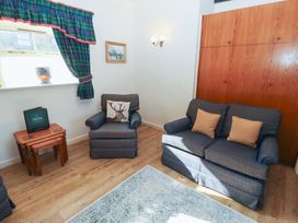 A room with a sofa and armchair with cushions a wooden side table with nested tables a window with tartan curtains and a wooden wardrobe at Bizzie Lizzie in Akeld near Wooler