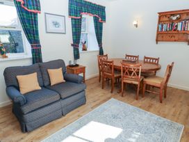 A room with a wooden dining table and chairs a blue upholstered loveseat with cushions curtains on windows a wooden side table and a bookshelf on the wall at Bizzie Lizzie Akeld near Wooler