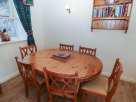 A dining room with a wooden oval table and six chairs a window with plaid curtains and a wooden bookshelf on the wall at Bizzie Lizzie in Akeld near Wooler