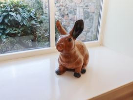 A wooden rabbit figurine on a white windowsill with a garden visible through the window at Bizzie Lizzie Akeld near Wooler