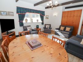A living room with a wooden dining table and chairs armchairs sofas a television and windows with curtains at Bizzie Lizzie in Akeld near Wooler