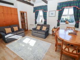 A sitting room with blue sofas a wooden dining table and chairs and windows with plaid curtains at Bizzie Lizzie in Akeld near Wooler