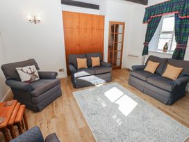 A sitting room with blue armchairs and sofas a wooden door and window with curtains at Bizzie Lizzie in Akeld near Wooler
