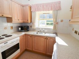 A kitchen with wooden cabinets a microwave an electric stove an oven a sink and a window with curtains at Bizzie Lizzie Akeld near Wooler