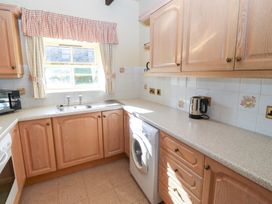 A kitchen with wooden cabinets a washing machine a stainless steel sink a kettle and a window with checked curtains at Bizzie Lizzie Akeld near Wooler