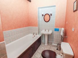 A bathroom with a bathtub a pedestal sink an oval mirror a toilet with a dark seat and a towel rack at Bizzie Lizzie Akeld near Wooler