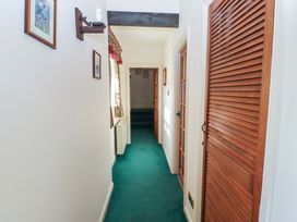A hallway with green carpet wooden louvered closet doors framed pictures and a window with floral curtains at Bizzie Lizzie Akeld near Wooler