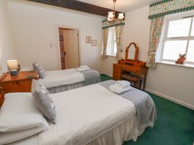 A bedroom with two single beds a wooden dressing table and windows with floral curtains at Bizzie Lizzie Akeld near Wooler