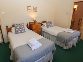 A bedroom with two single beds with grey sheep cushions and a wooden chest of drawers with a lamp at Bizzie Lizzie in Akeld near Wooler