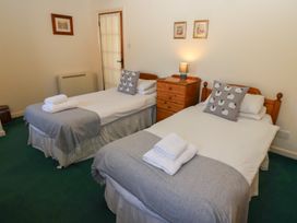 A bedroom with two single beds with gray throws and sheep pillows and a wooden chest of drawers with a lamp at Bizzie Lizzie in Akeld near Wooler