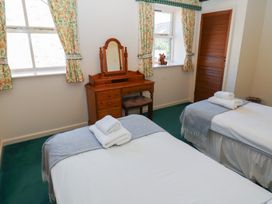 A bedroom with two single beds a wooden dressing table and floral curtains at Bizzie Lizzie in Akeld near Wooler