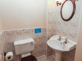 A bathroom with a toilet a pedestal sink an oval mirror and tiled walls at Bizzie Lizzie in Akeld near Wooler