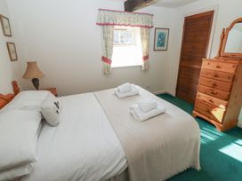 A bedroom with a bed with folded towels bedside lamp wooden dresser and window with floral curtains at Bizzie Lizzie Akeld near Wooler