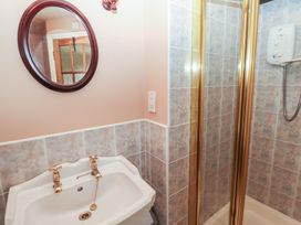 A bathroom with a white sink with brass taps and a round mirror above next to a tiled shower at Bizzie Lizzie Akeld near Wooler
