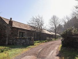 A stone building with windows along a gravel road next to leafless trees and greenery at Bizzie Lizzie in Akeld near Wooler