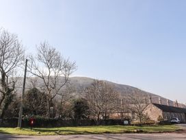 Stone cottages with bare trees and a grassy area in front with a hill in the background at Bizzie Lizzie Akeld near Wooler
