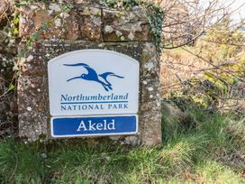 A stone sign with Northumberland National Park and Akeld text surrounded by grass and branches at Bizzie Lizzie Akeld near Wooler