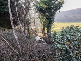 A small stream flowing through trees and bushes near open fields at Bizzie Lizzie in Akeld near Wooler