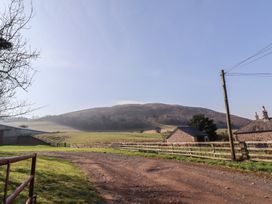 A gravel road leading to fenced fields with buildings and a hill in the background at Bizzie Lizzie Akeld near Wooler