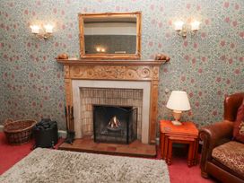 A fireplace with a fire and a mirror above it next to a table with a lamp and a leather armchair at Cheviot Manor in Akeld near Wooler