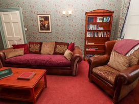 A sitting room with a sofa, armchair, wooden coffee table, bookshelf, and floral patterned wallpaper at Cheviot Manor in Akeld near Wooler