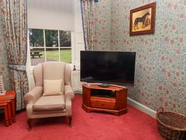 A beige armchair with a cushion next to a wooden TV stand and a flat screen TV in a room with floral wallpaper at Cheviot Manor in Akeld near Wooler