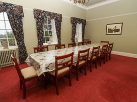 A dining room with a long table covered with a tablecloth and twelve chairs at Cheviot Manor in Akeld near Wooler
