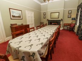 A dining room with a long table covered by a cloth with deer antler designs surrounded by wooden chairs and a fireplace at Cheviot Manor in Akeld near Wooler